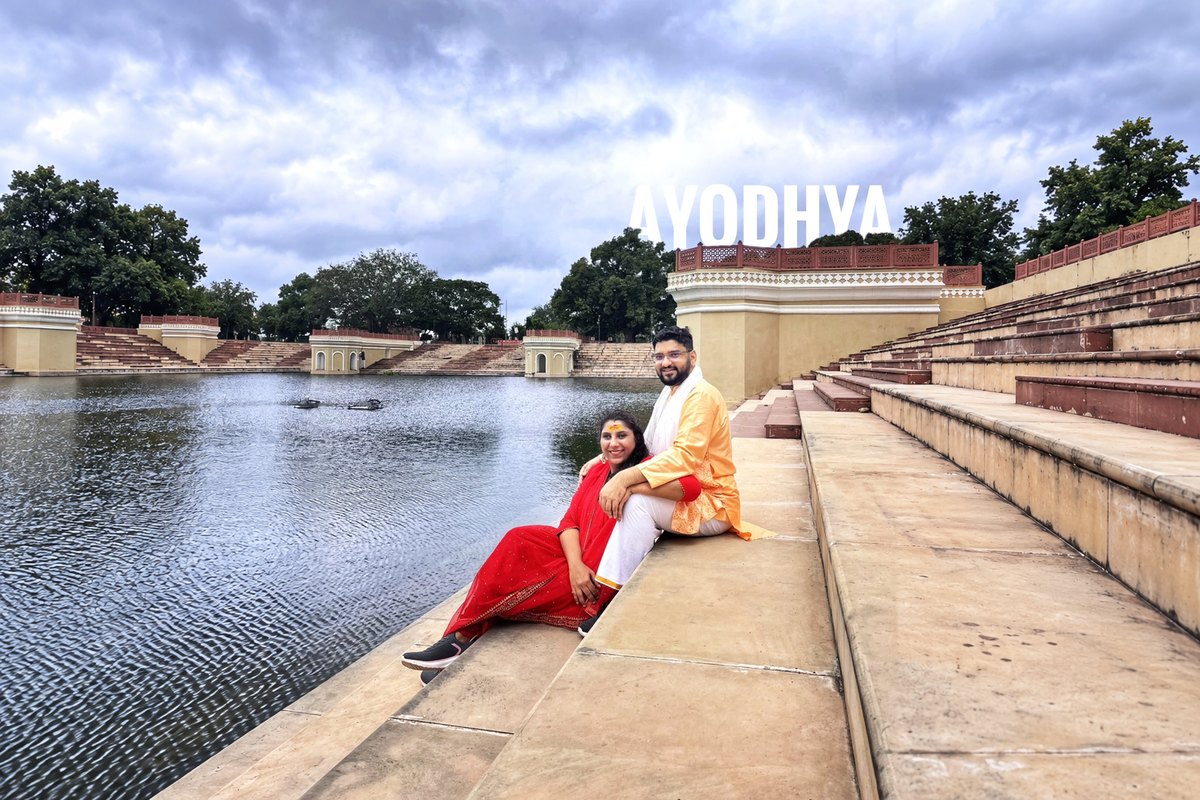 Saudamini and Shriram on the steps of a ghat in Ayodhya, AYODHYA written above the water