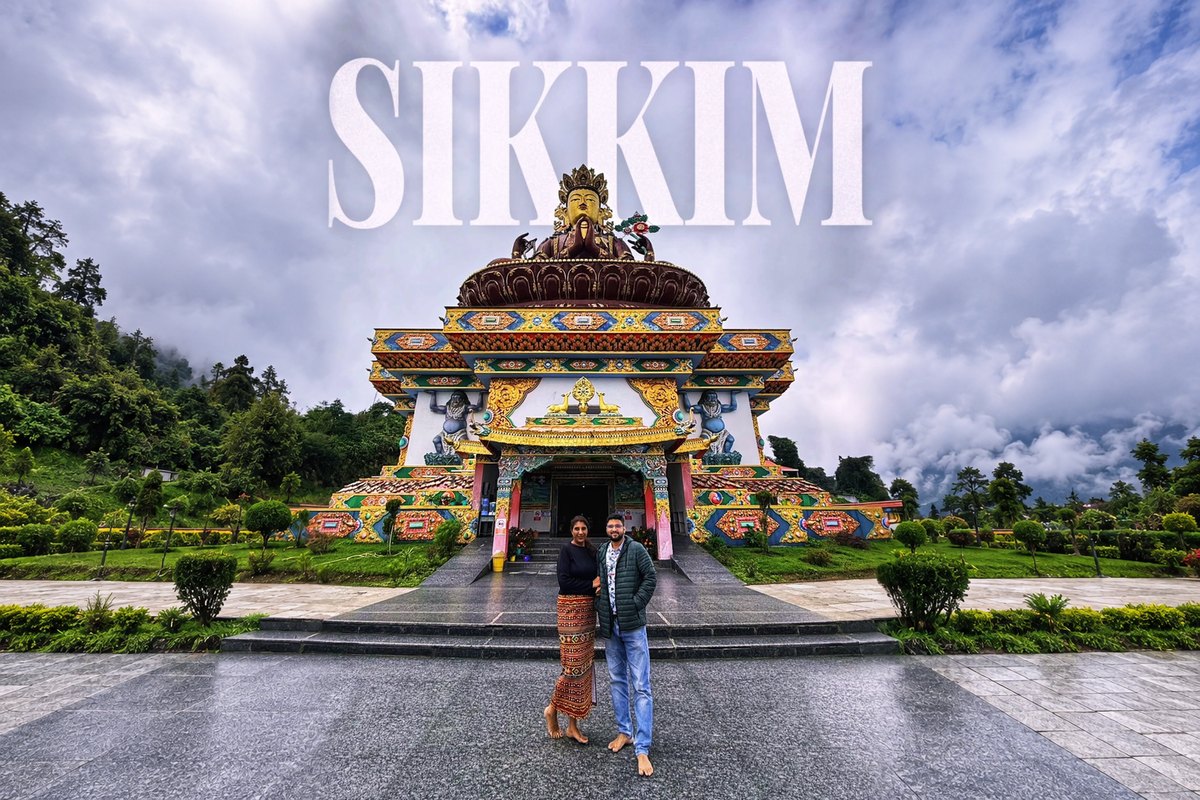 SIKKIM written across a cloudy sky above a monastery crowned by a giant golden Buddha