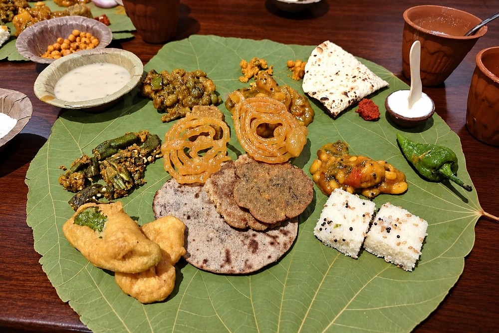 A Gujarati thali on a leaf plate at Vishala: jalebi, bajra rotla, white dhokla, chilli pakoras, bhindi, a roti and a fried green chilli, with clay cups on the side