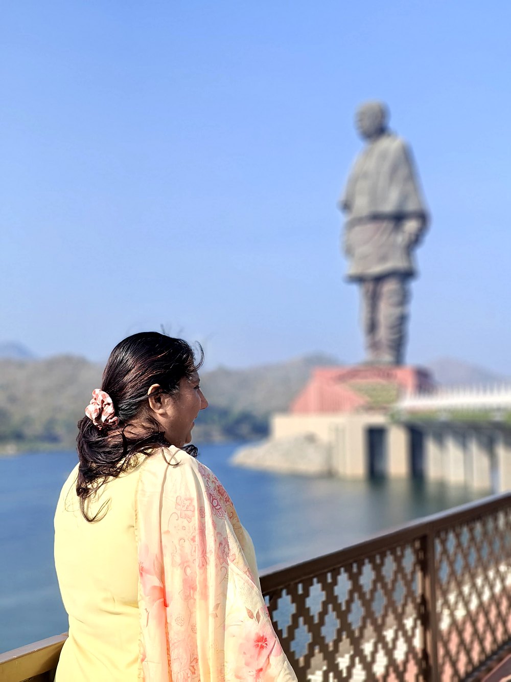 Saudamini at a railing by the Narmada, the Statue of Unity rising behind her