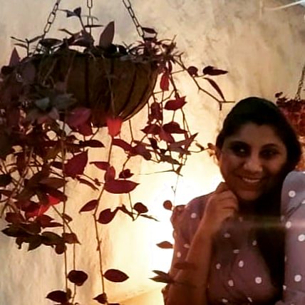 Smiling, beside a hanging plant lit warmly from below