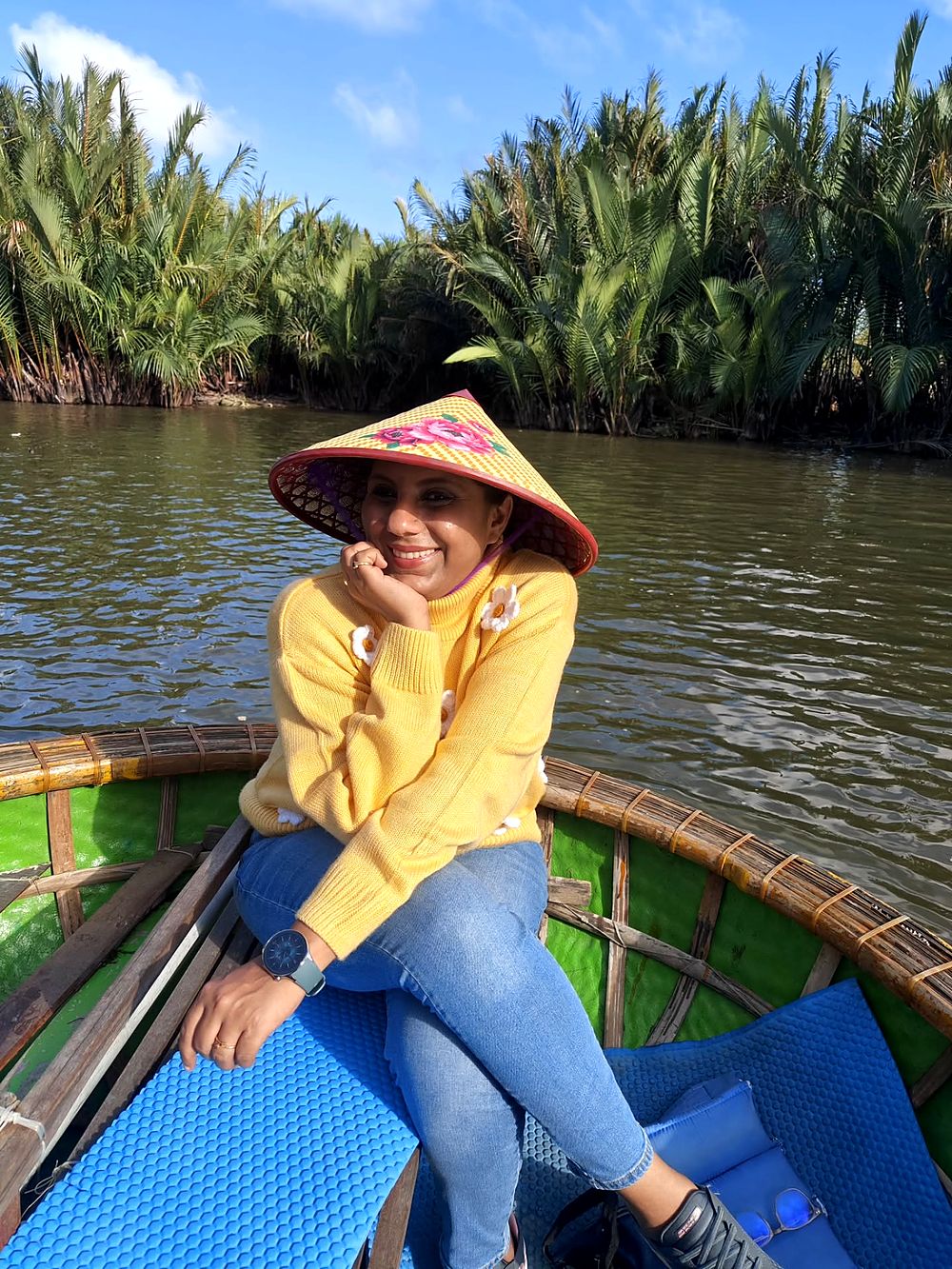 In a round coconut boat among the palms, wearing a conical hat